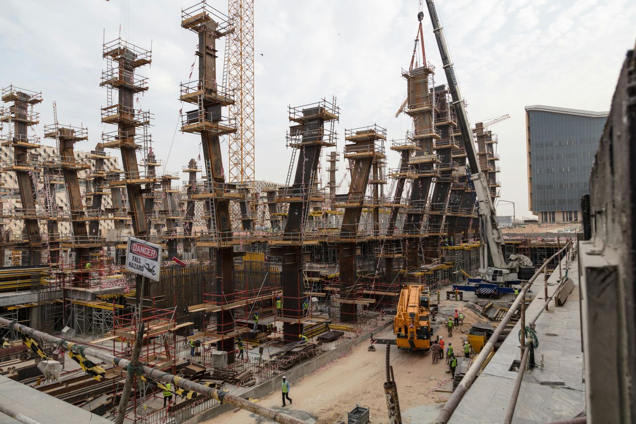 Home A bustling construction site with towering steel frameworks and cranes under a cloudy sky.